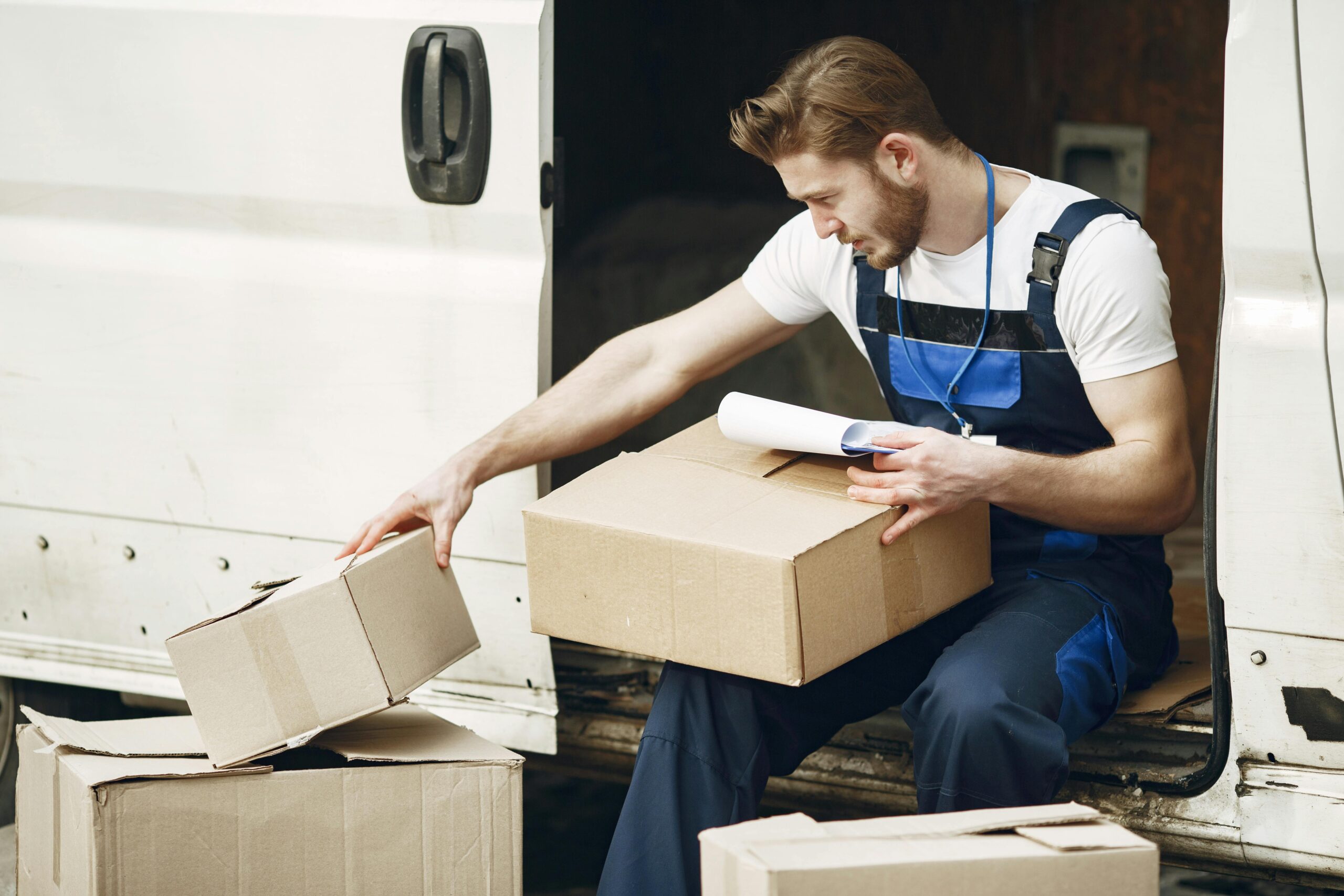 Courier organizing packages from a van, preparing for delivery in a logistics setting.